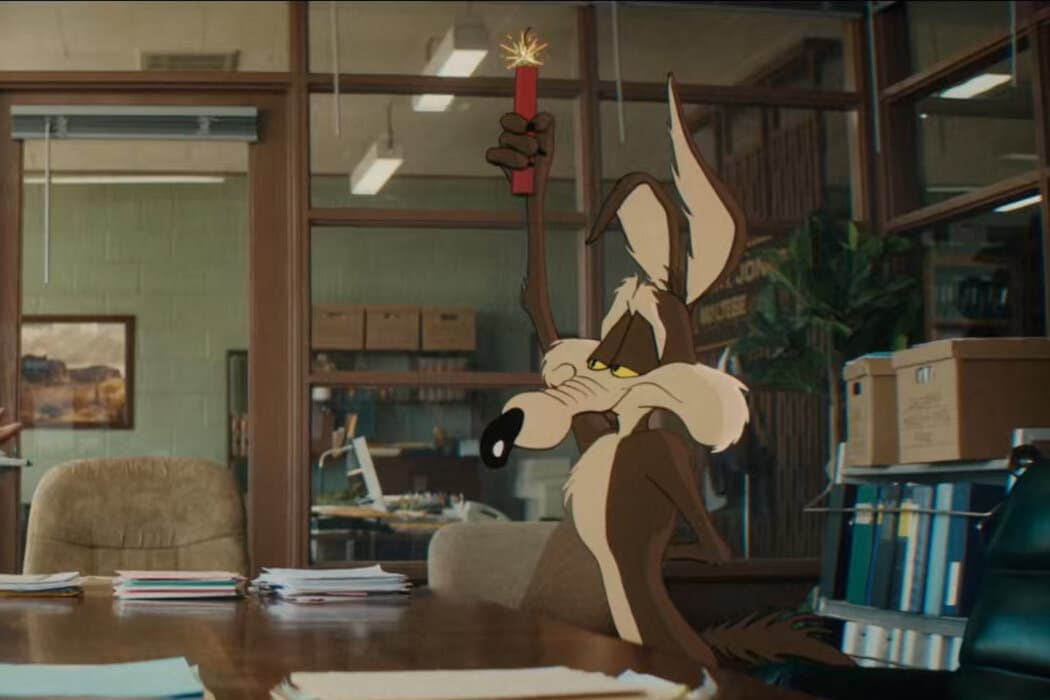 Animated Wile E. Coyote holds a lit stick of dynamite inside a live-action office in Coyote vs. Acme